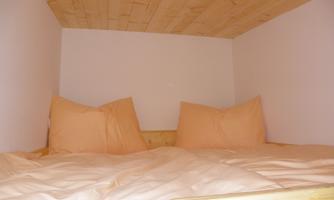 A cozy sleeping area with a wooden ceiling and large, comfortable pillows. The walls are bright and simple.
