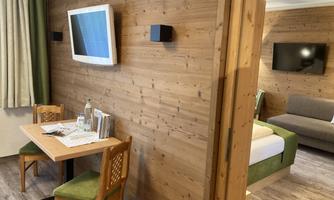 A cozy hotel room with wooden walls, a table and chairs. In the background, a sofa and two televisions can be seen.