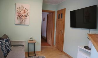 A cozy living room with a gray sofa and a television on the wall. A painting with floral motifs hangs on the wall.