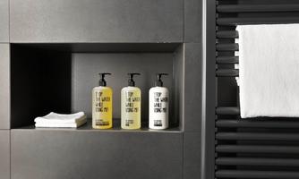 Three bottles of shower gel are on a shelf in a modern bathroom. Next to the bottles lie two white towels.