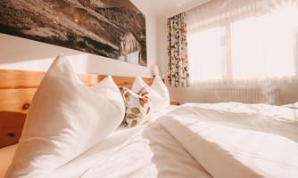 A cozy bedroom with a large bed and soft pillows. Sunlight streams through the window, creating an inviting atmosphere.