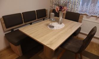 A cozy dining area with a wood-colored table and a bench-like seating arrangement. On the table, there is a vase with flowers and a candle holder.