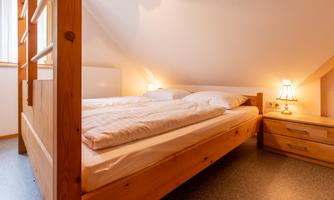 A cozy bedroom with a wooden double bed. Soft bedding and ambient lighting create a relaxed atmosphere.