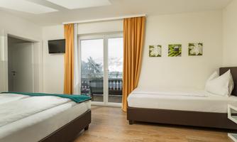 A modern bedroom with two beds and a balcony. The windows are covered with orange curtains, and the room has light wooden floors.