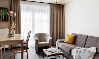 A modern living room with a gray sofa, an armchair, and a wooden table. Large windows let in plenty of light, and the curtains create a cozy atmosphere.