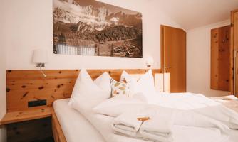 A cozy bedroom with a double bed and white pillows. An impressive picture of mountains hangs on the wall, and the room is bright and inviting.