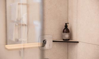 An elegant shower with a simple, modern shelf. On it rests a stylish soap dispenser.