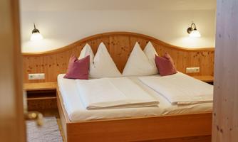 A cozy bedroom with a wooden frame bed and two pillows. Soft lamps are installed on the walls, creating a pleasant atmosphere.