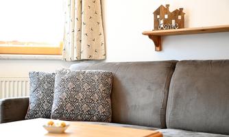 A cozy living room with a gray sofa and decorative pillows. On a shelf is a wooden sign with the inscription "Home".