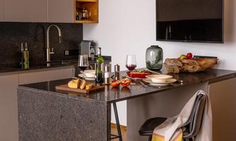 Modern kitchen with an elegant kitchen island and warm wooden elements. Plates and wine are on the table, while a blanket is casually draped over a chair.