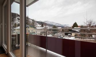 A balcony with a view of snow-covered mountains. The sky is gray and cloudy.