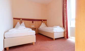 A simple room with two single beds and light carpet flooring. The walls are painted in soft colors and the window lets in a lot of light.