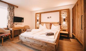 A cozy room with a large wooden bed and modern furniture. The walls are bright and the decor creates an inviting atmosphere.