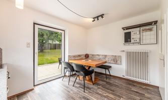A bright dining room with a wooden farmhouse table and black chairs. Large windows offer a view of the garden.