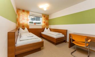 A bright room with two single beds and a desk. The walls are decorated with elegant patterns in green and orange.