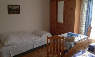 A simple room with a bed and a table.  
On the wall hangs a small picture, and there is a wardrobe as well as a curtain.