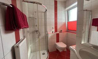 A modern bathroom with a shower and white tiles. Red towels and a large window create an inviting atmosphere.