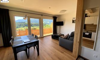 A cozy living and dining room with a table and a sofa. Large windows offer a beautiful view of the surrounding countryside.