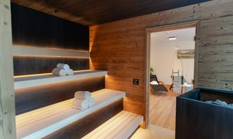 A modern wellness area with wooden shelves and stacked towels. In the background, a cozy room with a chair and plants is visible.