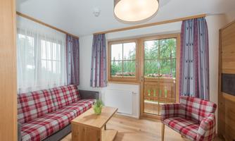 A cozy living or bedroom with a sofa and a chair in a checked design. Large windows provide a view of nature and bring in plenty of daylight.