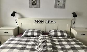 A cozy bedroom with a double bed and checked bed linens. Two pictures hang on the walls, and next to the bed are nightstands with table lamps.