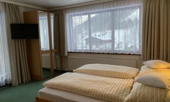 A cozy room with two beds, a TV, and large windows. Outside, a winter landscape can be seen.
