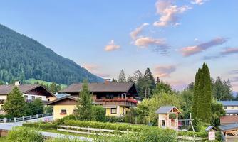An idyllic mountain landscape with cozy houses and lush greenery. The sky is colorful with soft clouds.