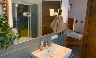 A modern bathroom with a shower, a sink, and a towel holder. In the background, part of a bedroom is visible.