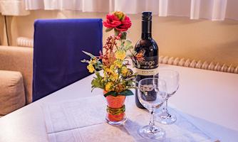A table with a bottle of wine, two glasses, and a colorful flower arrangement. The atmosphere is cozy and inviting.