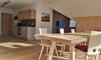 A modern kitchen with a dining area featuring wooden chairs and a large table. The rooms are bright and well-furnished.