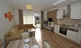 A modern apartment with a cozy sofa corner and an open kitchen area. Large windows with daylight and access to the terrace.