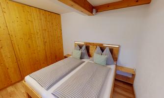 A cozy bedroom with a double bed and a wooden wardrobe. The pillows have a checkered pattern and add a warm atmosphere to the room.