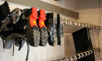 A shoe rack with various shoes, including red sports shoes and dark blue shoes. In the background, additional shoes and equipment are visible.