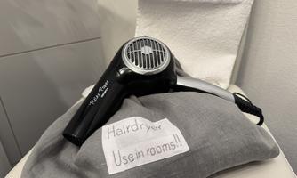 A hair dryer is lying on a gray fabric bag with a label. The bag indicates that the hair dryer can be used in the rooms.
