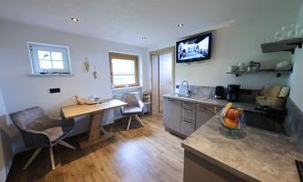 A modern kitchen with a dining table and comfortable chairs. The room is bright and inviting, with a television on the wall.
