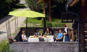 A group of people sits relaxed on a terrace and enjoys a meal outdoors. A parasol provides shade on a sunny day.