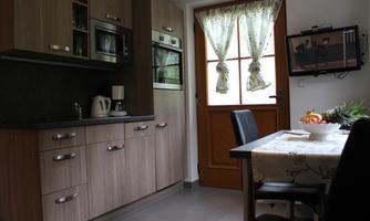 A cozy kitchen with modern wooden cabinets and a table decorated with fruit. The door to the outdoor area is open and adorned with curtains.