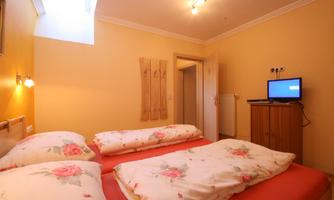 A cozy bedroom with two beds and yellow walls. A television and a bright light source create a pleasant atmosphere.