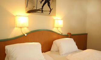 A cozy bedroom set with two beds and round nightstands. A picture of a skier hangs on the wall.
