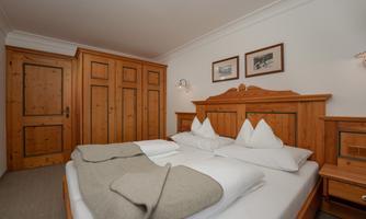 A cozy bedroom with wooden furniture and a large bed. Decorative pictures hang on the wall, and the room offers plenty of storage space.