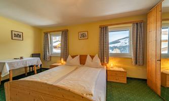 A cozy bedroom with a double bed and wooden furniture. Large windows offer a view of the snowy landscape.