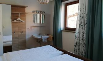 A cozy bedroom with a double bed and light bedding. There is a mirror on the wall, and the window is decorated with green curtains.
