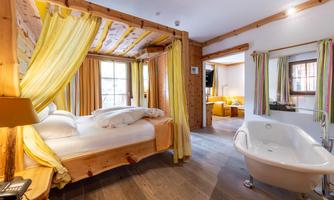 A cozy bedroom with a wooden bed and light curtains. The room features a freestanding bathtub and warm colors create an inviting atmosphere.