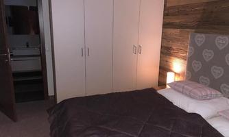 A cozy bedroom with a double bed and a large wardrobe. The wooden-clad wall gives the room a warm atmosphere.