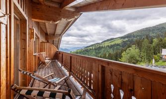 A cozy terrace with a wooden railing and deck chairs. In the background, green hills stretch out under a cloudy sky.