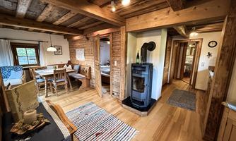 A cozy interior with wooden paneling and a stove. The room is bright and inviting, with a dining area and rugs.