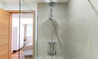 A modern shower with a glass wall and rain showerhead. The space is bright and designed in a minimalist style.