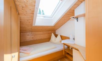 A cozy bedroom with wood paneling and a skylight. It is minimally furnished and offers a single bed as well as a small desk.
