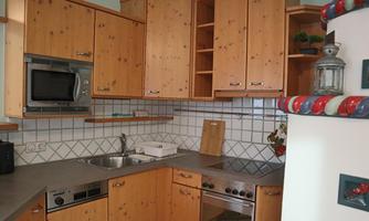 A cozy kitchen with wooden cabinets and modern appliances. The countertop is bright and clean, featuring a sink and a microwave.