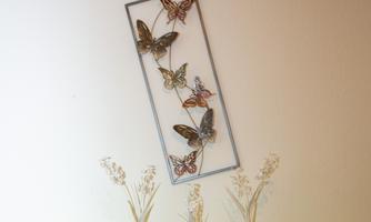 A decorative wall picture with colorful butterflies in a frame. Below it are three small vases with dried flowers on a light green surface.